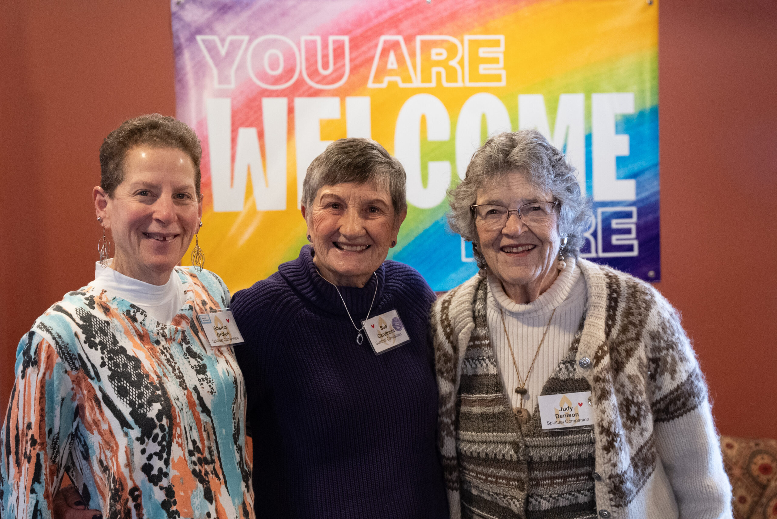 A few members of our pastoral care team stand smiling together in front of our "you are welcome" sign